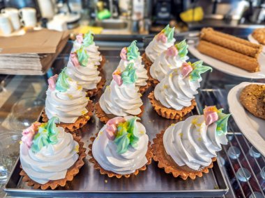 Pastane vitrininde beyaz kremalı turtalar ve renkli dekoratif çiçekler sergileniyor..