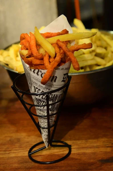 French fries close up. Belgian potatoes in vintage newspaper. Traditional fast food - fried potatoes. Large bowl with fried potatoes in the background Fries Sweet Orange Potato