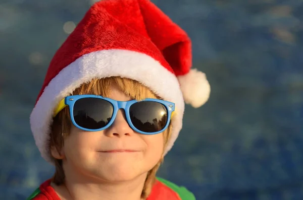 Portret Uroczego Chłopca Kapeluszu Świętego Mikołaja Okularach Przeciwsłonecznych Tle Basenu — Zdjęcie stockowe