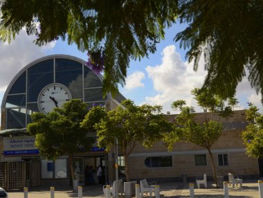 İsrail. Netivod, Kasım 2022. Negev Çölü 'ndeki tren istasyonu. İstasyon binası, büyük bir saat ve çiçek açan bir jakaranda..