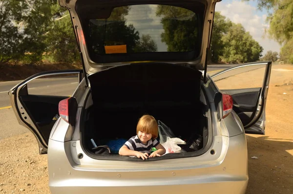A little boy is sitting in the trunk of a car. Concept: family car trip, holidays with children