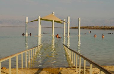 İsmail. Ölü deniz Ein Bobek. Kasım 2022. Halka açık plajlar ve yüzen insanlar. Tuz gölünde. Sağlık tatili - İsrail sağlık merkezi güneş şemsiyeleri