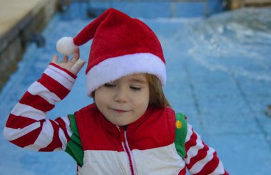 Havuzun ya da fıskiyenin arkasında Noel Baba şapkalı şirin bir çocuğun portresi. Kavram: Tropikal Noel, kış yolculuğu, kışın yaz.. 