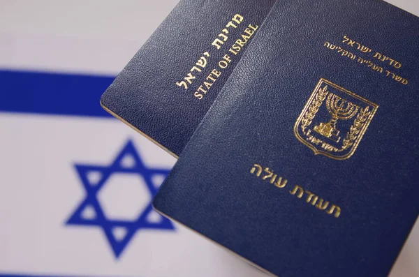 An international biometric passport of a citizen of Israel and a passport of a new immigrant against the background of the flag of Israel. TRANSLATION: Teudat ole. Concept: Immigration to Israel
