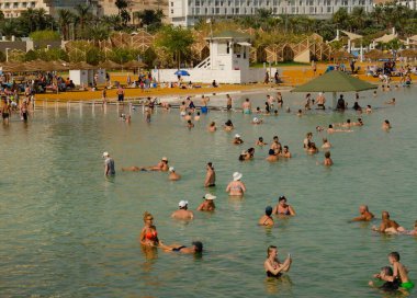 İsmail. Ölü deniz Ein Bobek. Kasım 2022. Halka açık plajlar ve yüzen insanlar. İsrail sağlık merkezi. Terapötik çamur ve tuzlu su dağları ve arka planda lüks oteller.