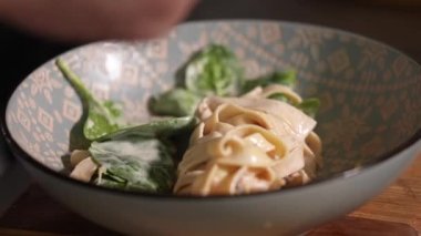 Makarna ve şampiyonlarla dolu tabak. Şefin eli fesleğeni bitmiş tabağa koyar. Restoranda yemek servisi. Ağır çekim. İtalyan yemeği. fettuccine ve mantar