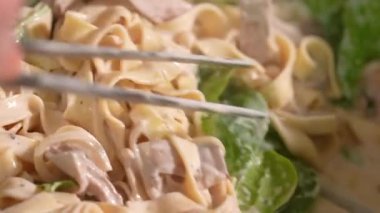 İtalyan makarnası pişirmek. Şampiyonlarla karıştırılmış Fettuccine ve fesleğenli krema. Şef makarna maşasıyla makarnayı karıştırır. Yakın çekim, iştah açıcı ağır çekim.