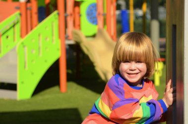 Çocuk parkında renkli bir kazak giyen sevimli bir çocuk. Çocuk gülüyor, oynuyor, kaydırak kayıyor. Çocuk tatili, eğlence parkı, tatiller, aile tatili, anaokulu kavramı..