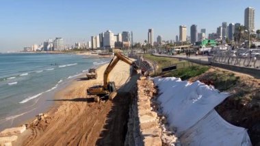 Tel Aviv 'de. İsrail. Aralık 2022. Kumsaldaki kazıcı Hyundai büyük taşlar, kayalar yüklüyor. Arka planda kum ve deniz var. Tel Aviv Panoraması.