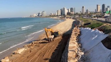 Tel Aviv 'de. İsrail. Aralık 2022. Kumsaldaki kazıcı Hyundai büyük taşlar, kayalar yüklüyor. Arka planda kum ve deniz var. Tel Aviv Panoraması.