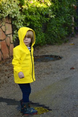 Yağmurda bir çocuğun portresi. Sarı yağmurluk ve kapüşonlu bir çocuk, gülüyor ve gülümsüyor. Yağmurda yürürken, su geçirmezken