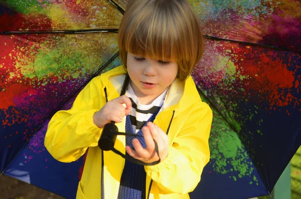 A cute boy in a yellow raincoat, a portrait of a child under a bright multi-colored umbrella. Concept: bad weather, good mood, kindergarten, autumn, spring.