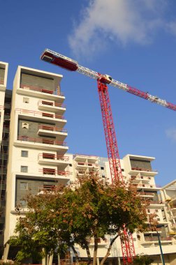 Bir inşaat alanı, beyaz bir bina ve uzun bir inşaat vinci. Geliştirme endüstrisi. Ev almak, ipotek. Modern konut binaları. Metin için boşluk, mavi gökyüzü, yaz