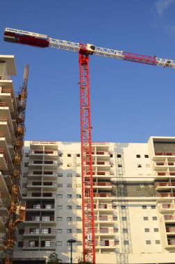 Bir inşaat alanı, beyaz bir bina ve uzun bir inşaat vinci. Geliştirme endüstrisi. Ev almak, ipotek. Modern konut binaları. Metin için boşluk, mavi gökyüzü, yaz