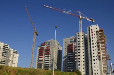 Bir inşaat alanı, beyaz bir bina ve uzun bir inşaat vinci. Geliştirme endüstrisi. Ev almak, ipotek. Modern konut binaları. Metin için boşluk, mavi gökyüzü, yaz