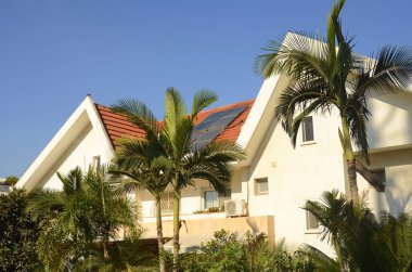 Tropikal bir ülkede güneş panelleri. Güzel villa, palmiye ağaçları ve çatıdaki güneş panelleri. Kavram: enerji krizi, kaynak tasarrufu, yenilenebilir enerji kaynakları