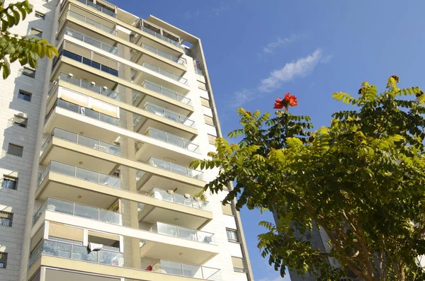 A cozy white balcony in an apartment high-rise building. Blooming African tulip tree near the house. City garden, public garden. Apartment rent, apartment purchase, realtor, investment, mortgage.