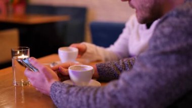 The guy and the girl drink coffee at the bar, the guy scrolls the phone. Smartphone in the hands of a man. Friendly conversation.