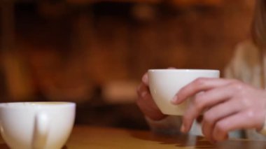 The girl drinks coffee, fresh espresso in a white cup. Hands and lips are close-up, the face is not visible. A conversation in a coffee shop, a friendly meeting, a date.