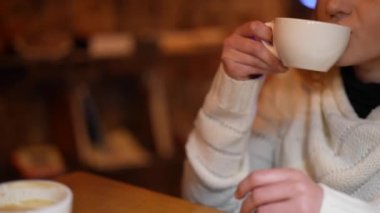 The girl drinks coffee, fresh espresso in a white cup. Hands and lips are close-up, the face is not visible. A conversation in a coffee shop, a friendly meeting, a date.