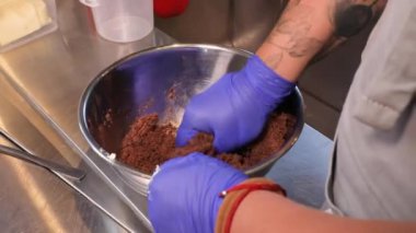 Close-up - hands in rubber gloves. Cooking brownies, chocolate cake. Chef's hands are kneading chocolate dough.