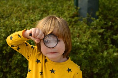 Küçük çocuk bir büyüteç tutuyor. Çocuk ilginç bir şey arıyor. Kavram: ara.