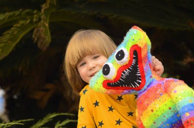 A positive little boy, 4 years old, walks in the park with a bright colored toy. Concept: kindergarten, imaginary friend, favorite toy.