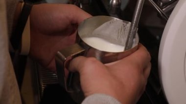 Latte hazırlığı. Kahve makinesi köpüren süttür. Barista 'nın elleri bir sürahi sütü tutuyor..