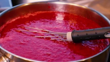 The process of making berry jam. The hand adds sugar and stirs the jam with a whisk. Strawberry raspberry jam.
