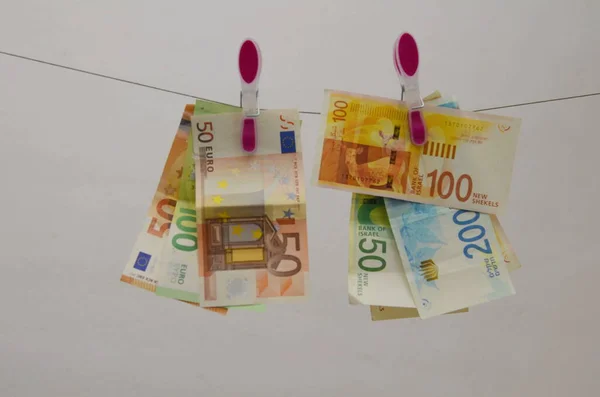 Concept: the Israeli shekel against the dollar and the euro. Cash New Israeli Shekel, American Dollar, Euro. Paper banknotes hang on clothespins. Concept: taxes, exchange rate, investment, savings, profit.