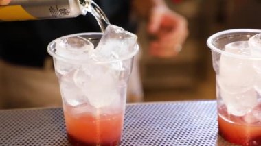 Preparation of a cocktail with ice and grenadine, close-up hand pours tonic into a plastic cup. Red syrup and clear tonic. takeaway cocktail