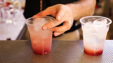 Preparation of a cocktail with ice and grenadine, close-up hand pours tonic into a plastic cup. Red syrup and clear tonic. takeaway cocktail