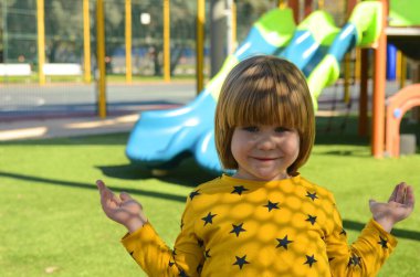 Front view of small caucasian boy four years on playground. The boy smiles and laughs. Portrait of a child on a walk. A boy in a yellow sweater on the background of a slide