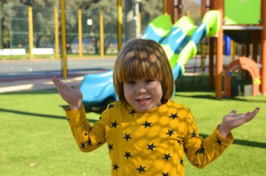 Front view of small caucasian boy four years on playground. The boy smiles and laughs. Portrait of a child on a walk. A boy in a yellow sweater on the background of a slide