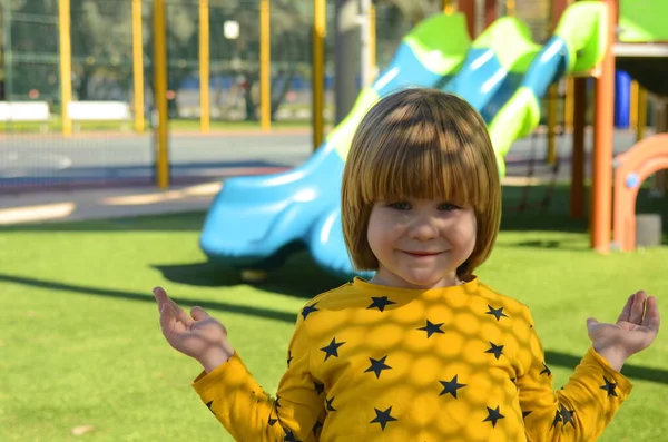 Front view of small caucasian boy four years on playground. The boy smiles and laughs. Portrait of a child on a walk. A boy in a yellow sweater on the background of a slide