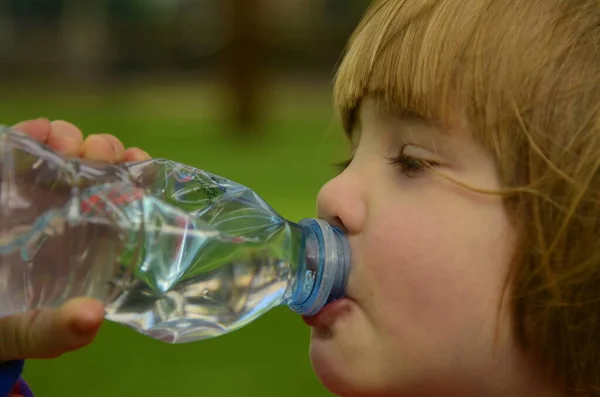 Little boy drinks from a plastic bottle. Concept: summer, thirst, plastic.