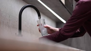 A man's hand holds a glass, water flows from the tap in the kitchen. Glass with clean water. Concept: Tap water, drinking water ecology, water filters