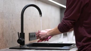 A man cleans the faucet and sink in the kitchen with a sponge. Concept: keeping clean, man cleans, cleaning space.