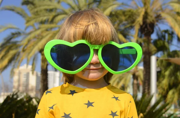 stock image A cute boy in large glasses in the shape of a heart. The child rejoices in the holiday. Concept: Mother's Day, Purim, carnival, going to the circus, entertainment park. Traveling with children a symbol of love and hugs.