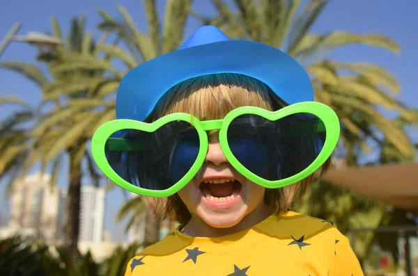 stock image A cute boy in large glasses in the shape of a heart. The child rejoices in the holiday. Concept: Mother's Day, Purim, carnival, going to the circus, entertainment park. Traveling with children a symbol of love and hugs.