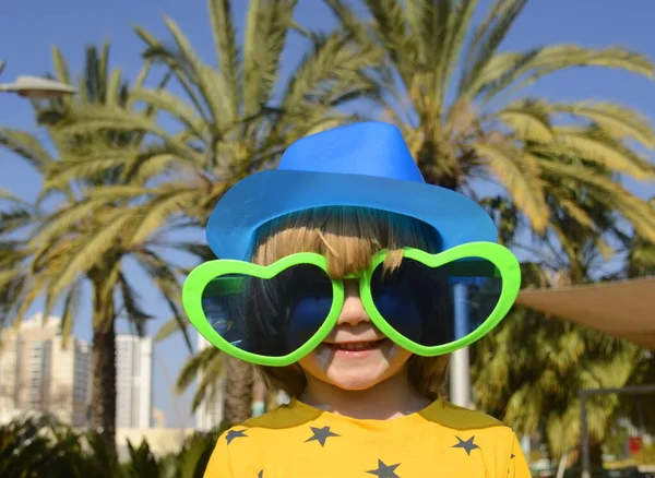 stock image A cute boy in large glasses in the shape of a heart. The child rejoices in the holiday. Concept: Mother's Day, Purim, carnival, going to the circus, entertainment park. Traveling with children a symbol of love and hugs.