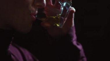Karanlıktaki adamın yüzü. Bir adam bardaktan sarı bir sıvı içer. Adam limonata ve enerji içeceği içiyor..