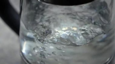 Elektrikli cam çaydanlık su kaynatır. Ölçme kolonu, su miktarı. Yavaş çekim çaydanlığı. Kaynama işlemi. Yakın çekim, guruldayan sıcak su, çaydanlık ışığı