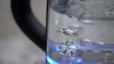 Elektrikli cam çaydanlık su kaynatır. Ölçme kolonu, su miktarı. Yavaş çekim çaydanlığı. Kaynama işlemi. Yakın çekim, guruldayan sıcak su, çaydanlık ışığı