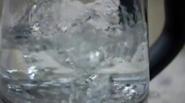 Elektrikli cam çaydanlık su kaynatır. Ölçme kolonu, su miktarı. Yavaş çekim çaydanlığı. Kaynama işlemi. Yakın çekim, guruldayan sıcak su, çaydanlık ışığı