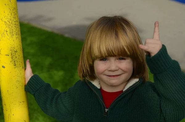 一个长发 穿着绿色毛衣的英俊男孩的画像 那孩子举起了手 — 图库照片