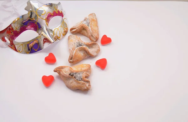 Kartpostal Purim. Beyaz arka planda karnaval maskesi ve hamantashen kurabiyeleri