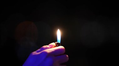 Karanlıkta bir adamın eli çakmak tutar. Arka planda şehir ışıkları.