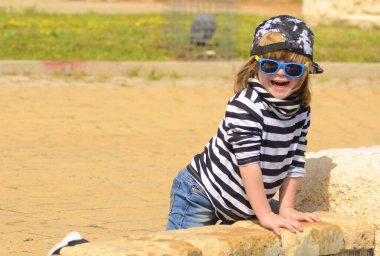 Çizgili tişörtlü ve güneş gözlüklü havalı bir çocuk. 4 yaşında bir çocuk parkta koşup dans ediyor. Aktif pozitif çocuk. Keyfin yerinde yaz..