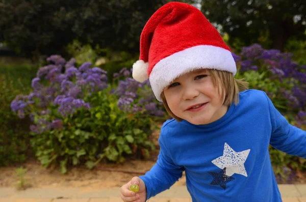 Mały Chłopiec Kwitnącym Ogrodzie Kapeluszu Świętego Mikołaja Koncepcja Boże Narodzenie — Zdjęcie stockowe